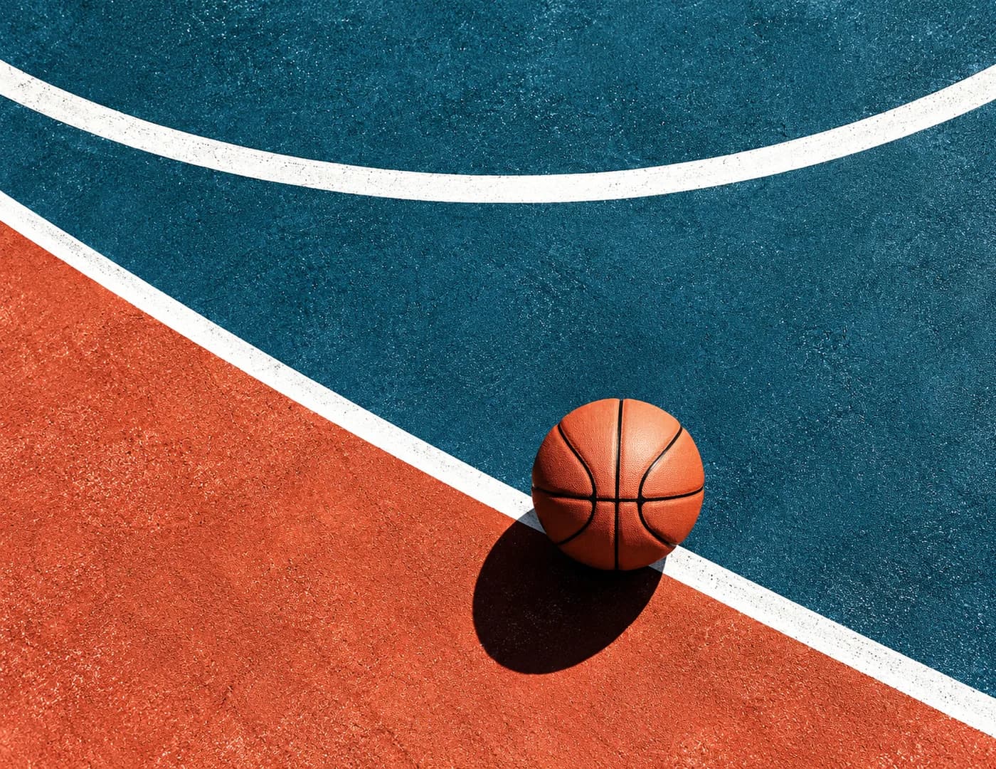Basketball liegt von oben gesehen auf einem rot-blauen Court mit weißen Linien und Schatten