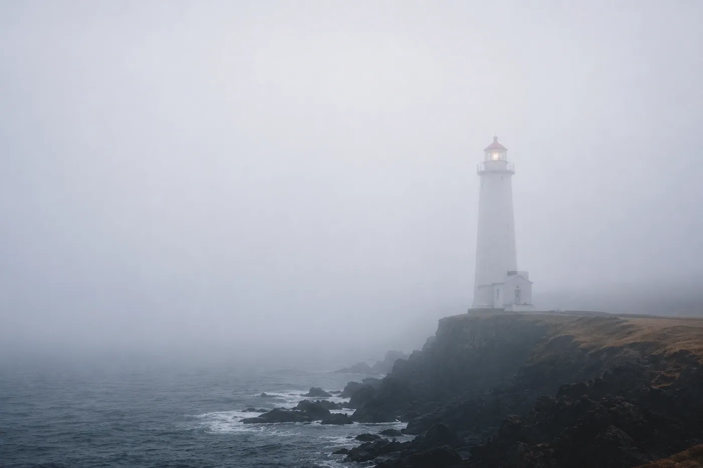 Ein einsamer Leuchtturm steht auf einer felsigen Küste im Nebel