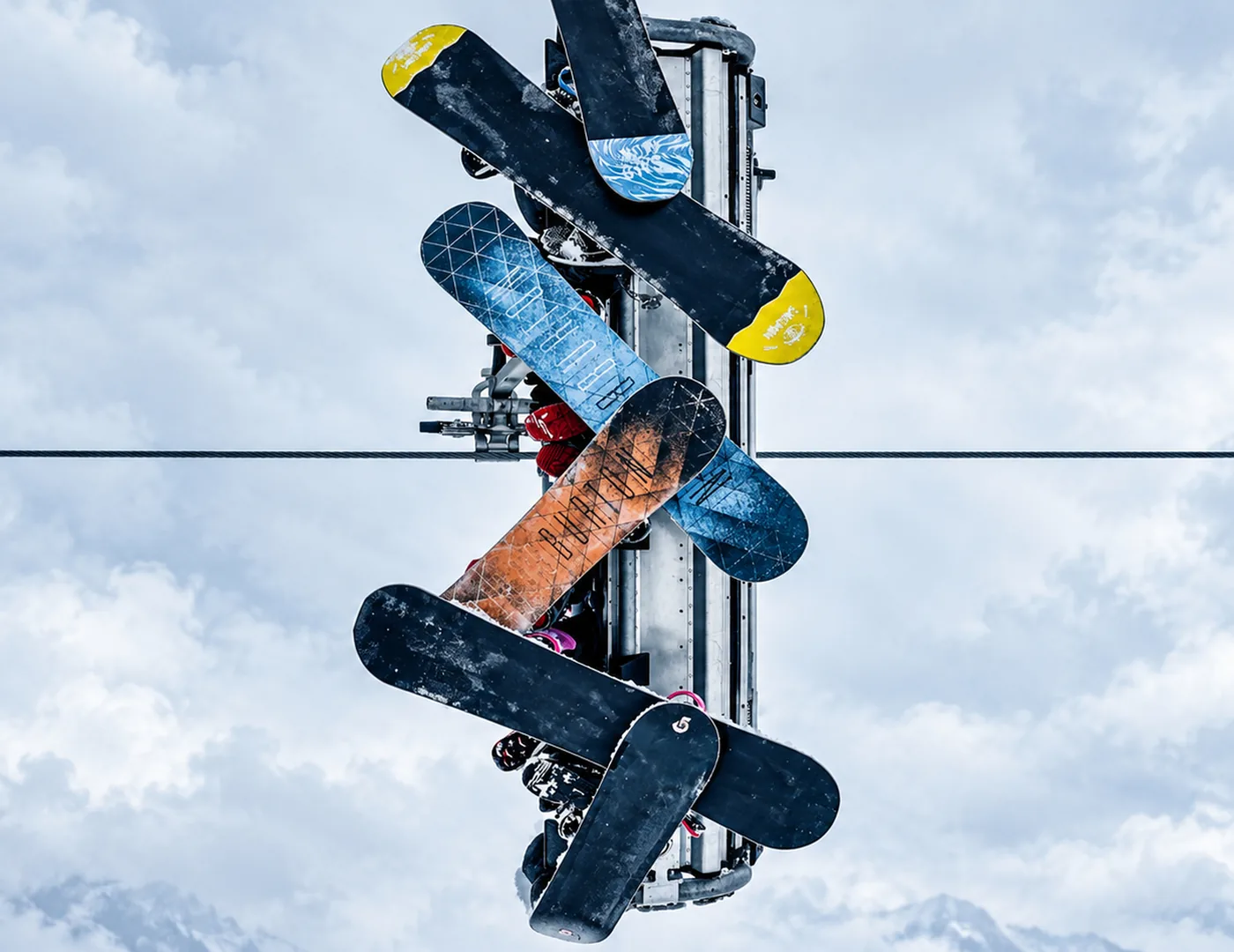 Von unten gesehen hängen Snowboards an einem Sessellift vor einem Himmel mit Wolken.